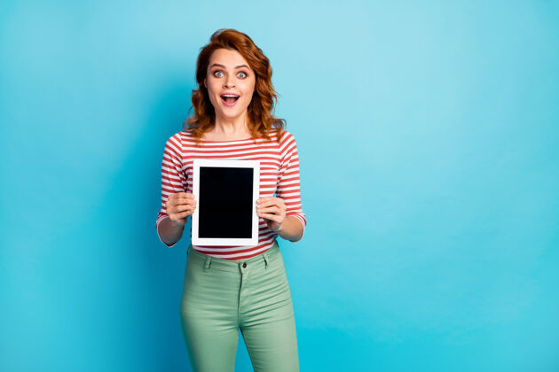 惊喜令人惊讶的时髦女人的肖像拿着新的平板电脑她展示新的现代科技新奇尖叫哇omg穿时尚套头衫隔离蓝色广告屏幕示范