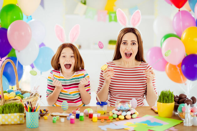 女性两个可爱迷人的狂喜疯狂的创意开朗活泼的小女孩的画像小妹妹戴着兔子耳朵在白色灯光的室内房间玩工艺品吹有趣孩子