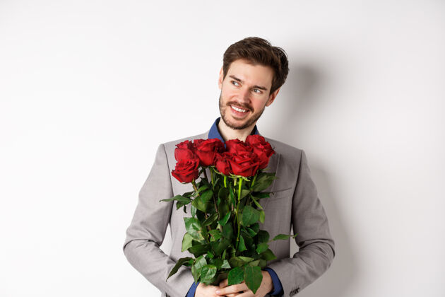 情感迷人的笑脸男人去浪漫的约会 穿着西装 捧着一束玫瑰 左顾右盼 站在情人节礼物白色背景关系同性恋情人节