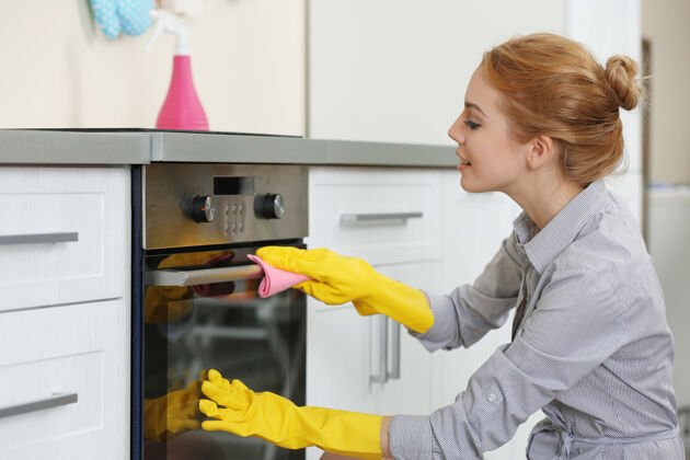 家政年轻的女人在厨房清洗烤箱清洗家庭主妇橱柜