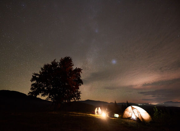 宇宙一群游客带着吉他在星空下燃起篝火与银河星座相映成趣露营帐篷生活方式