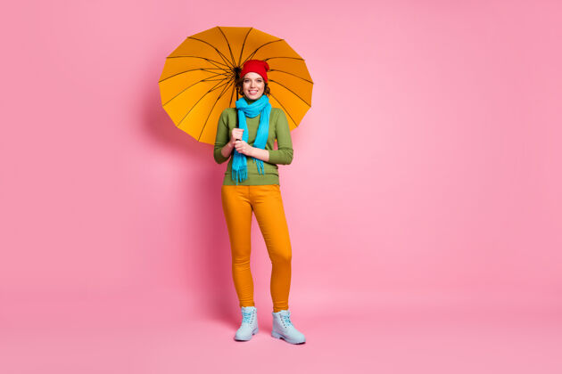 季节开朗可爱可爱漂亮女孩的全尺寸照片享受暴雨旅游假期手持明亮的雨伞穿着休闲风格的套装套头衫隔离在粉红色的墙上时尚套头衫休闲
