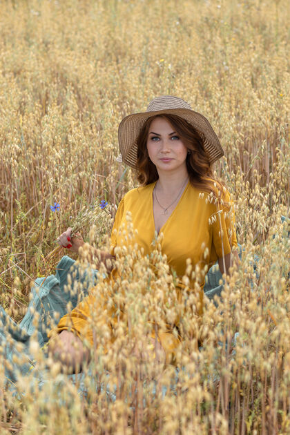 太阳在一个阳光明媚的夏日 一位年轻漂亮的孕妇穿着黄色的裙子 戴着黄色的帽子 走过一片麦田天空风景自然