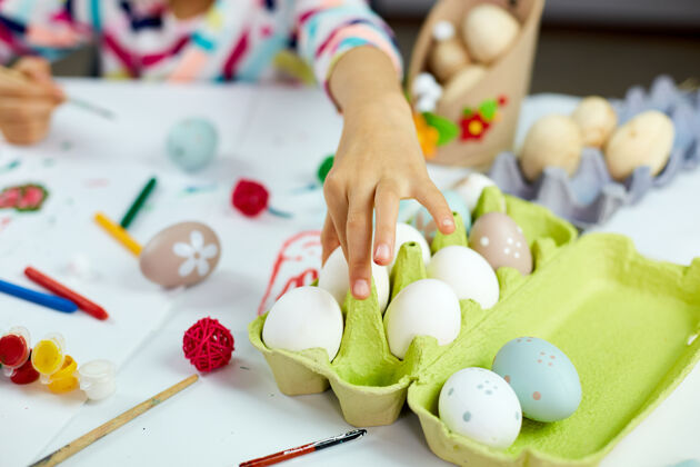 季节认不出来的小女孩拿着鸡蛋 在家里画画 用毛笔画鸡蛋孩子准备复活节 玩得开心 庆祝节日复活节快乐 diy小女孩色彩复活节