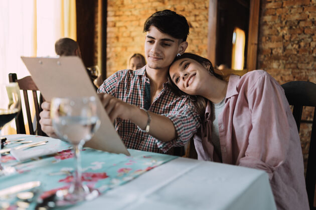庆祝美丽的年轻夫妇在餐厅看菜单决定情侣决定