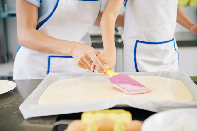 甜点特写图片的母亲帮助女儿分发液体面团在烤板用硅胶抹刀蛋糕烘焙家庭主妇