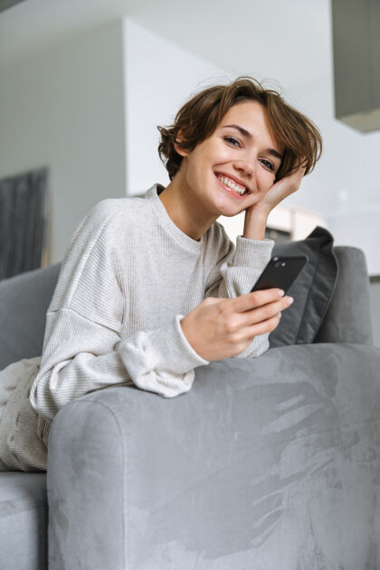 室内快乐的年轻女子坐在家里的沙发上 用手机自由职业者手机信息