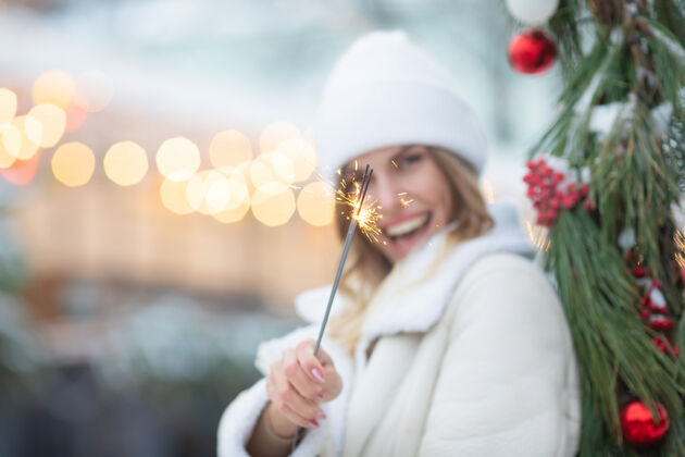 城市年轻美丽快乐微笑的女孩手捧火花 走在路上的户外照片街上的女人穿着时髦的冬天衣服圣诞节新年 概念户外欢呼博览会