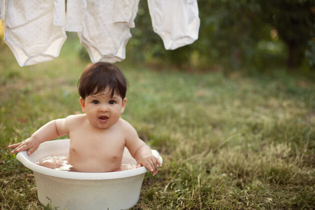 湿日落时分 男婴在院子里的盆里洗澡放松坐童年