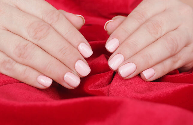 皱巴巴的美丽的美甲和柔软的粉红色指甲油在皱巴巴的红色天鹅绒上的女性手红色手手指