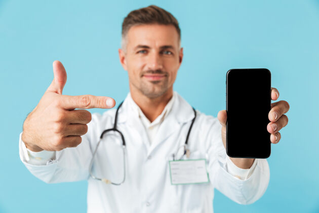 治疗专业医生身穿白大褂 手持听诊器手持手机 孤零零地站在蓝色墙壁上的照片工人诊所治疗