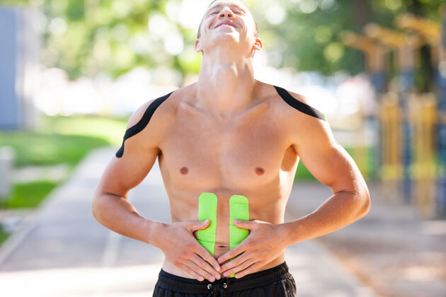 男人帅气的年轻白种人专业健美运动员的肖像 在运动场上 身体接触腹部的弹性运动带理疗身体治疗