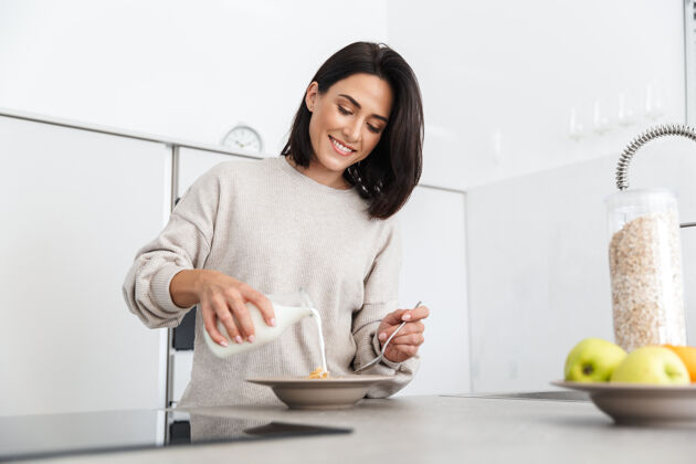 室内30多岁的成熟女人站在家里的现代厨房里 一边用燕麦片和水果做早餐景点成人吃