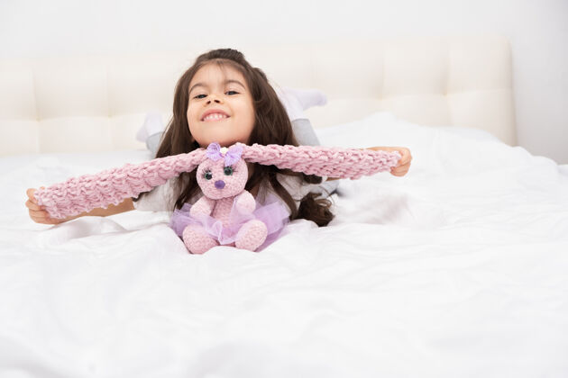 泰迪穿着家装的小女孩和泰迪兔坐在家里的床上就寝时间童年正宗