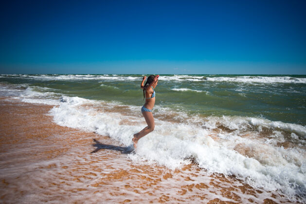 运动在一个阳光明媚 温暖的夏日里 快乐活泼的小女孩在狂风暴雨的海浪上跳跃想象沙滩阳光