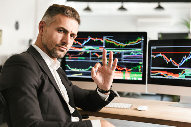 吸引力30多岁的商人穿着西装在电脑上工作 屏幕上有图形和图表主管财务数据
