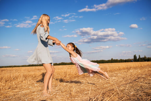 户外快乐的年轻母亲正在给她可爱的小女儿纺纱田地小麦欢呼