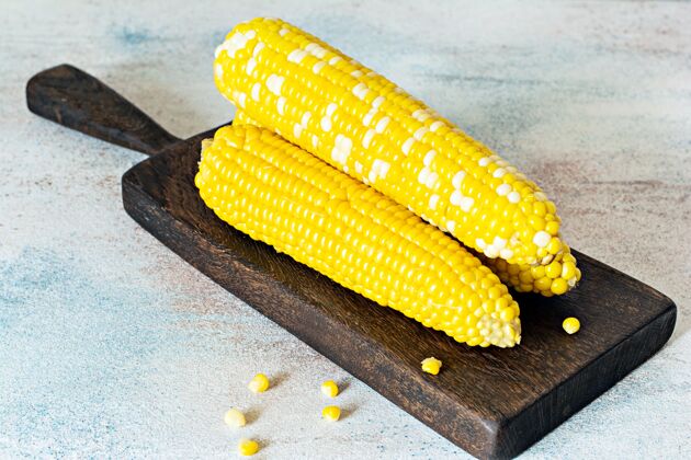 小吃在灰色（蓝色）背景的木板上放上新鲜煮熟的（煮熟的）玉米成熟的玉米成熟热健康