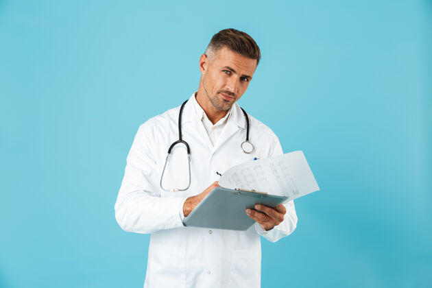 专家欧洲医生手持听诊器手持健康卡 孤零零地站在蓝色墙壁上的画像职业白种人肖像