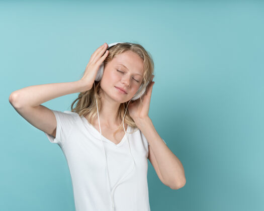 蓝色通过耳机收听音乐的年轻女子的肖像 颜色为中性色调的浅绿色音乐闭着眼睛年轻