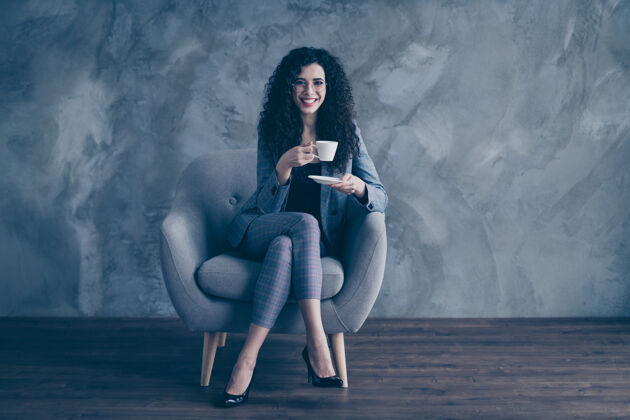 年轻商务女士坐在椅子上喝着热咖啡隔着灰墙背景职业工作正装