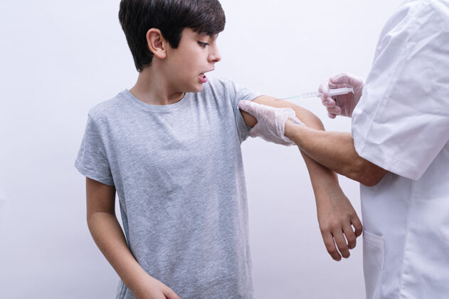 诊断一位戴着白色乳胶手套的护士在给卷发男孩注射疫苗的时候抓住他的肩膀注射器愈合疾病