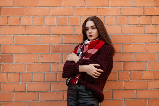 毛衣身穿紫红色毛衣和黑色皮裤的年轻女子站在城市的砖墙附近女孩衣服紧身裤