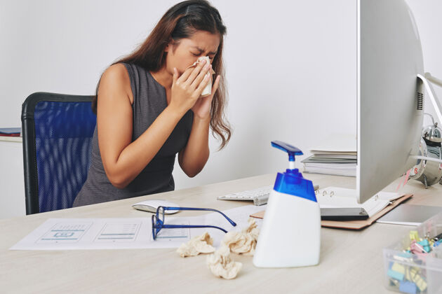 电脑年轻的女商人坐在办公桌前用纸巾打喷嚏 流感和过敏的概念过敏商务女性商务人士