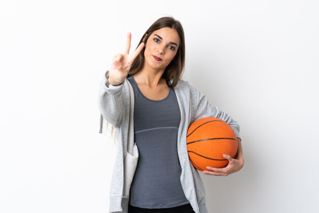 爱好年轻女子打篮球时脸上带着白色的微笑和胜利的标志健康女人运动