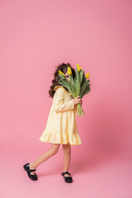 孩子粉红工作室里一个穿着黄色连衣裙的微笑女孩背景欢快郁金香花束快乐的孩子礼物时尚庆祝