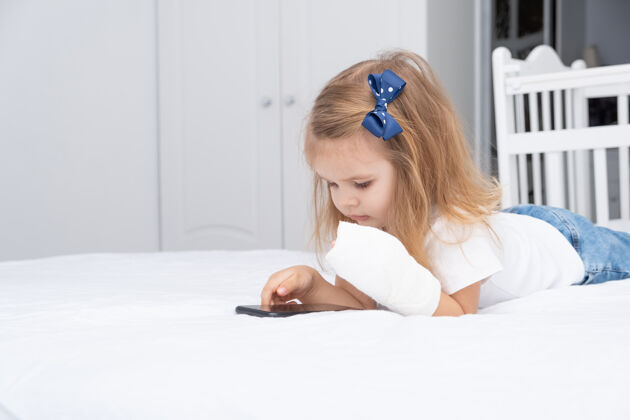 疼痛手拿石膏的小女孩躺在床上用智能手机 看动画片或教育视频医疗石膏房子