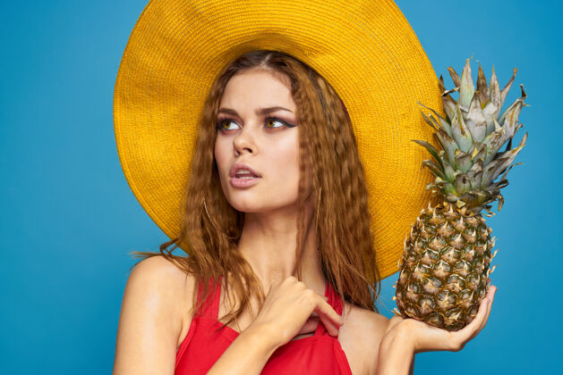 魅力戴着黄色帽子的女人 手里拿着菠萝 心情愉悦 生活方式 夏日水果蓝墙帽子鸡尾酒时尚