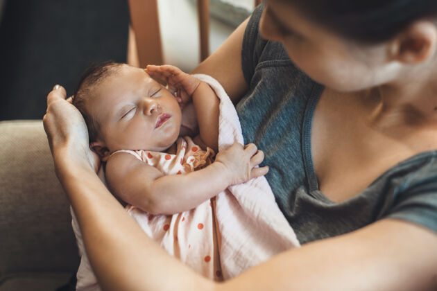 新生儿上图：一位长着雀斑的白人母亲抱着刚出生的婴儿 用被子盖着婴儿拥抱发展