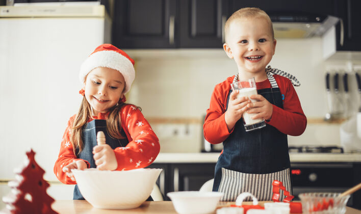 乐趣快乐的妹妹穿着圣诞老人的衣服在厨房里做饭吮吸味道孩子