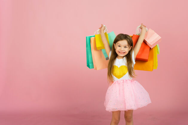 商业金发碧眼的小女孩喜欢在淡粉色的背景上购物copyspace.sale.cute文件小女孩在工作室里带着许多五颜六色的购物袋女孩裙子童年