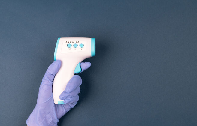 发热手戴手套 手持深蓝色背景的红外温度计远距离温度检查技术流感扫描仪