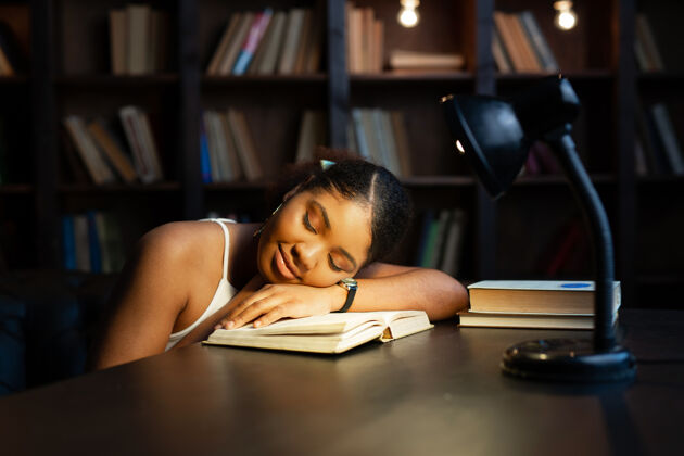 肖像年轻漂亮的非洲女人和书一起睡在桌边学习文学大学