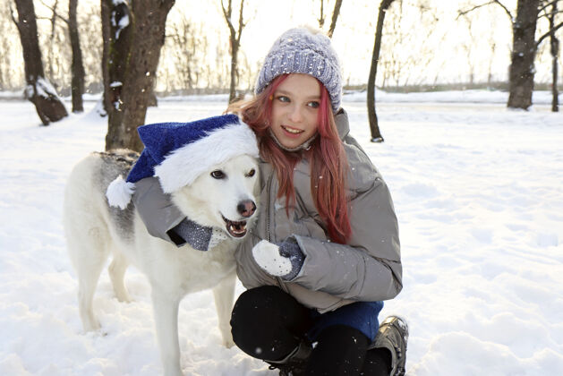 雪这个女孩在冬天愉快地与大自然中戴着圣诞老人帽子的狗交流冬天天气配件