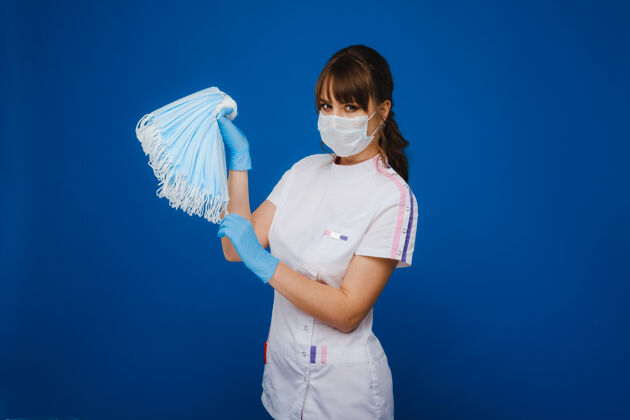 湿巾一个戴着医用口罩的年轻女医生手里拿着很多口罩一个护士在蓝色背景上摆姿势打喷嚏家庭作业衣服