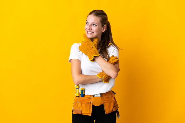 修理年轻的女电工隔离在黄色背景下向旁边看眼睛木匠商业