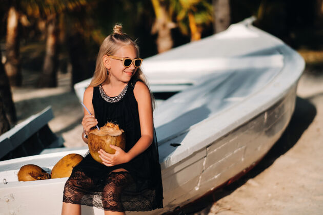 放松海滩上一个可爱的小女孩一边放松一边吃椰子海滩上一个女孩在一条船旁边 手里拿着一个小男孩毛里求斯椰子小岛海洋风景热带