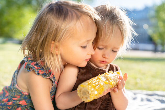 健康两个快乐的小男孩女孩妹妹在夏天吃甜玉米芯白天健康吃饭 野餐黄脸女孩