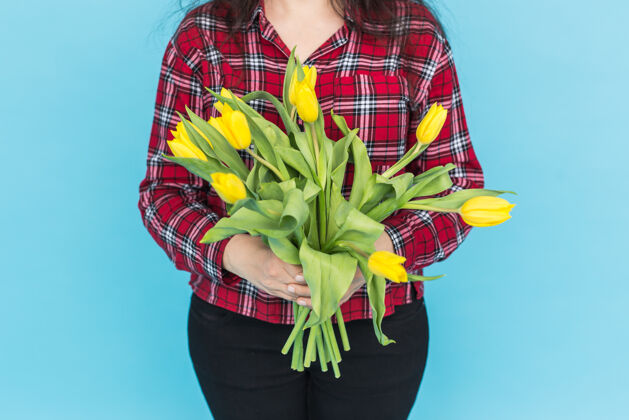 庆祝一束黄色的郁金香在女人的手上 在蓝色的表面向上花春天