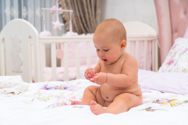 肖像一个快乐的胖乎乎的 没穿衣服的小女婴在托儿所的小床上玩耍 这是一张特写照片玩耍裸露兴趣