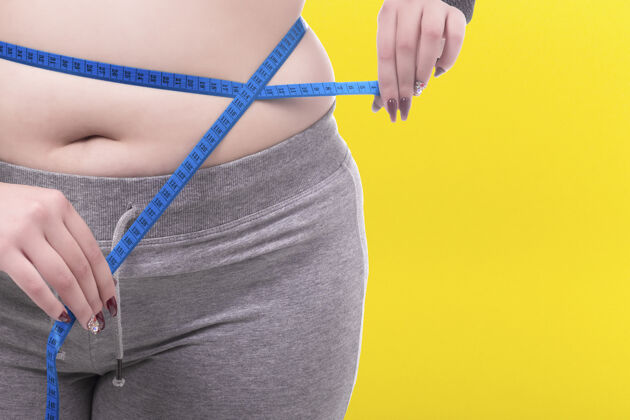 体重黄色背景上测量腰围的加大码女人护理人超重
