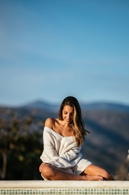 休闲穿着柔软毛衣的积极女性微笑着闭上眼睛 在模糊的山峦背景下 在院子里的边界上放松毛衣休息服装