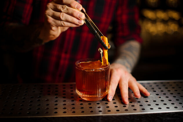 夜生活吧台上的酒吧招待用新鲜橘皮威士忌装饰鸡尾酒杯饮料配料酒吧