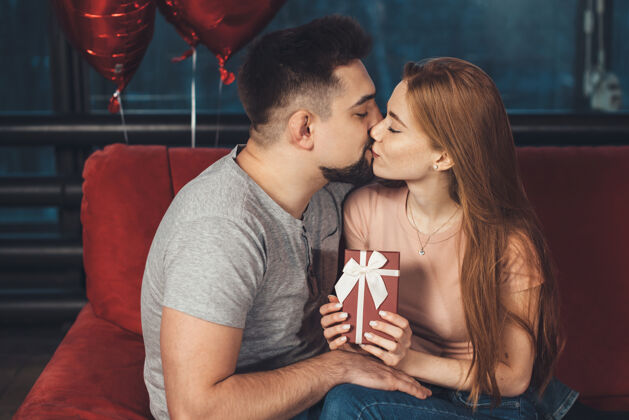 关系在情人节那天 一个高加索姜女在红色沙发上摆姿势 收到礼物后亲吻她的爱人女性男人丈夫
