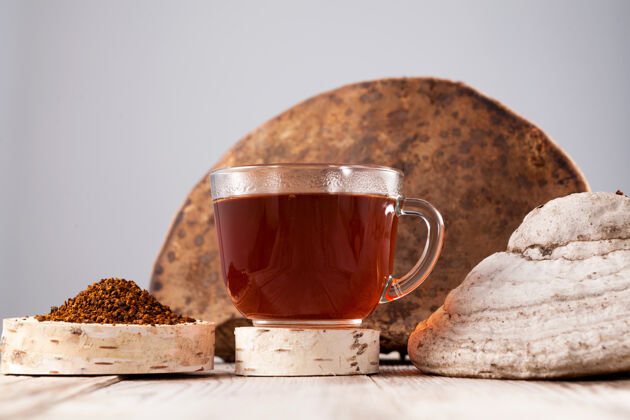 超级食品茶-一个强大的抗氧化剂 增强免疫系统 有排毒的质量 提高免疫力消化健康在一个干净的杯子里喝 旁边是一个完整的桦树蘑菇和磨碎的粉末乡村杯子树皮