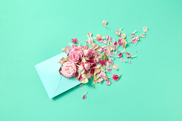 花束带有手工信封的祝贺卡 绿松石色背景上有新鲜的玫瑰和花瓣 复印件空格.top查看粉彩花花朵